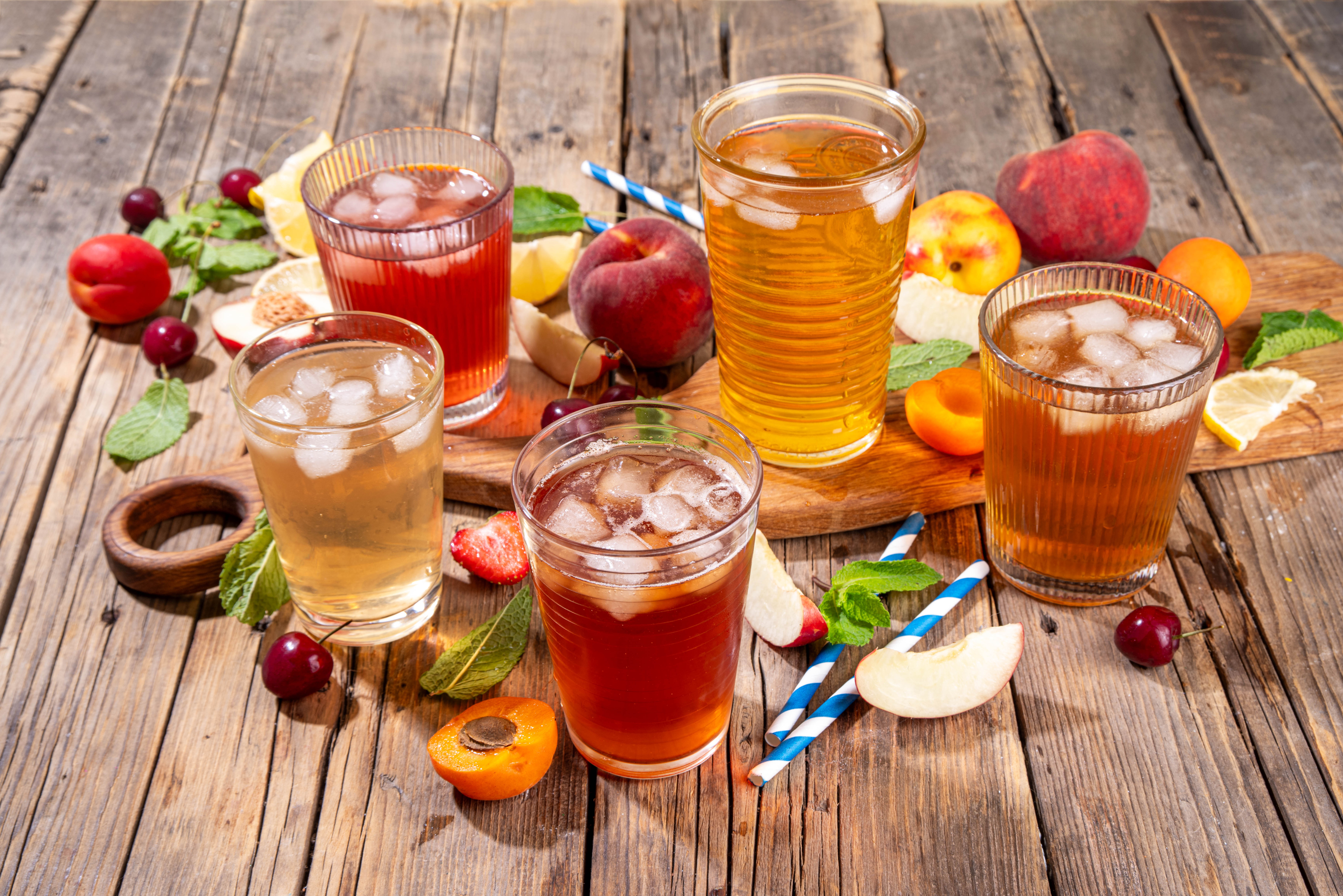 Summer refreshing drink, non alcohol tea based cocktails, iced tea varieties in different glasses, with fruit juices - strawberry, peach, apricot, cherry cold tea on wooden cozy background
