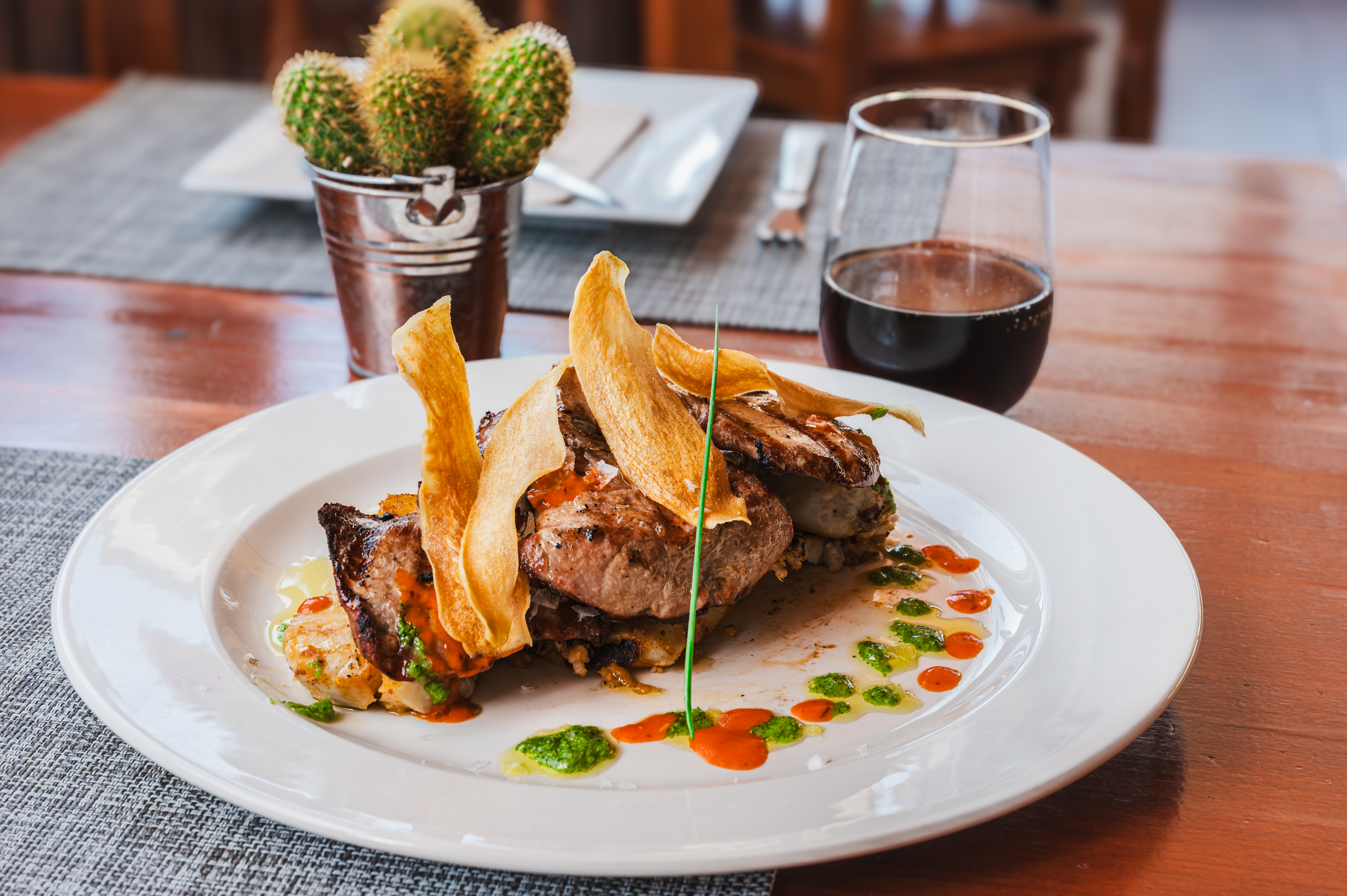 A grilled tuna steak is plated with crisp yuca chips and dots of red and green mojo sauce. Canarian fine dining for restaurant menus and island food tourism.